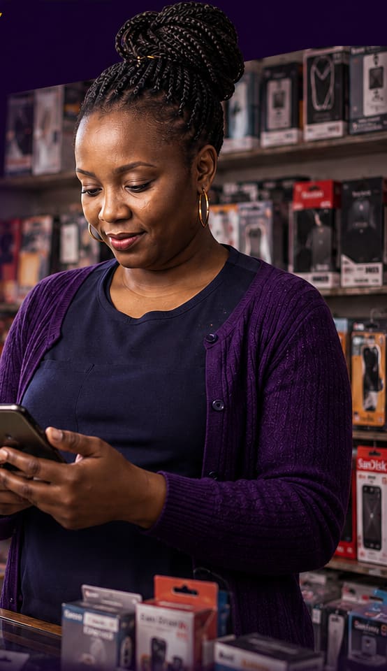 A shop owner behind her counter, confirming a customer's payment on her phone before handing over the goods.
